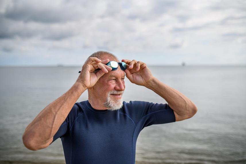 A man holding his goggles on his forehead, a body of water in the background